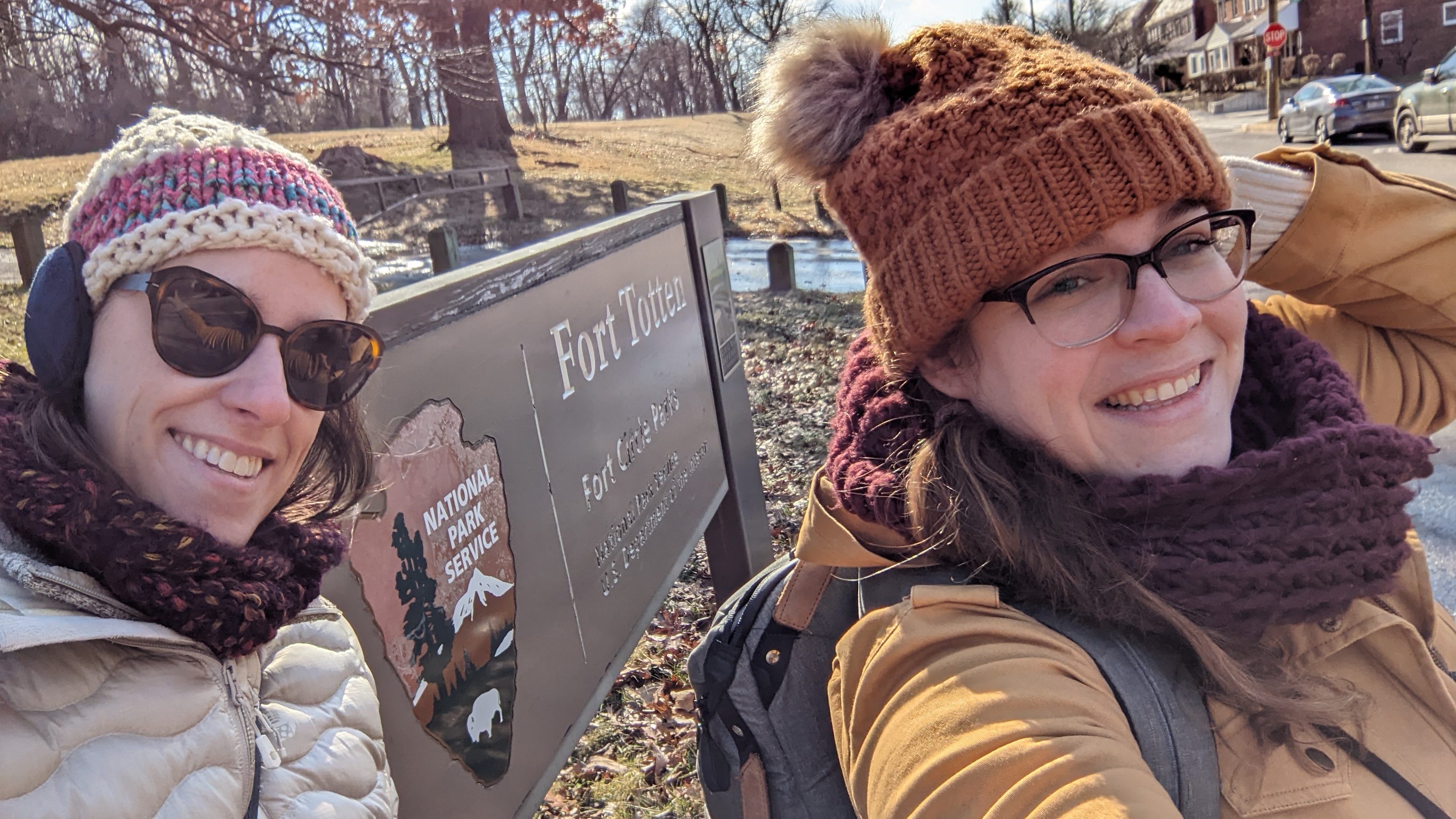 Two friends pose with the Fort Totten park sign on a cold day. 
